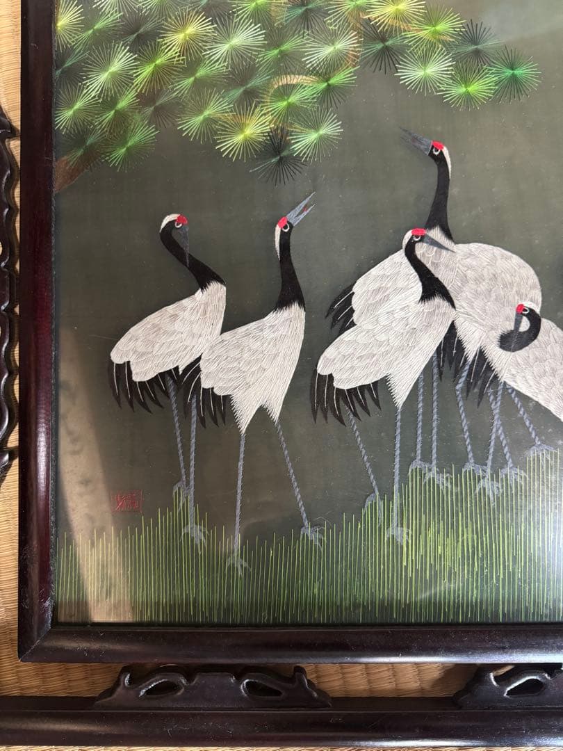 鶴の群れと松の木がデザインされた、額入りの手刺繍のアートワーク